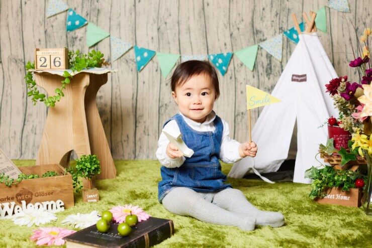 赤ちゃんが緑色の絨毯の上でポーズを取り、にこやかにほほ笑んでいるFamm無料撮影会の光景